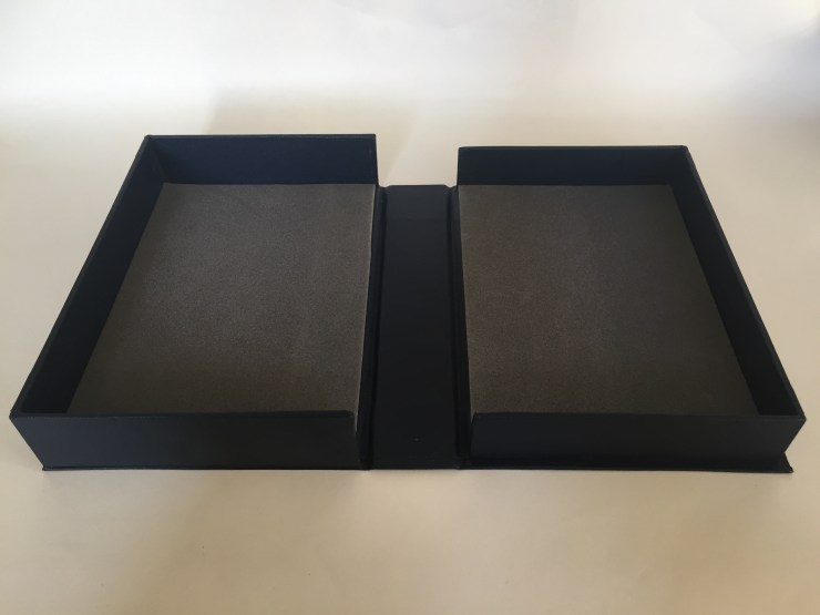 Image of a clamshell or drop spine box made from millboard and covered in blue bookcloth opened flat on a surface