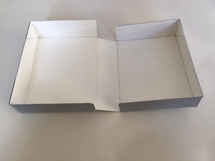 Image of a clamshell or drop spine box made from corrugated board opened flat on a surface